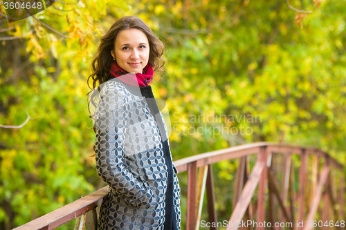 Image of Half-length portrait of a beautiful young girl standing on the bridge against the backdrop of autumn leaves yellow