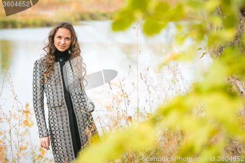 Image of Portrait of a young girl on the background of autumn river with blurred leaves in the foreground