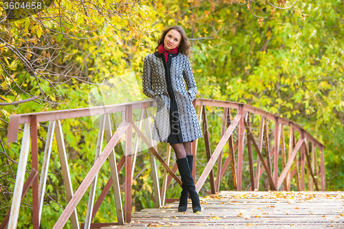 Image of A young girl stands on the bridge of a warm autumn day