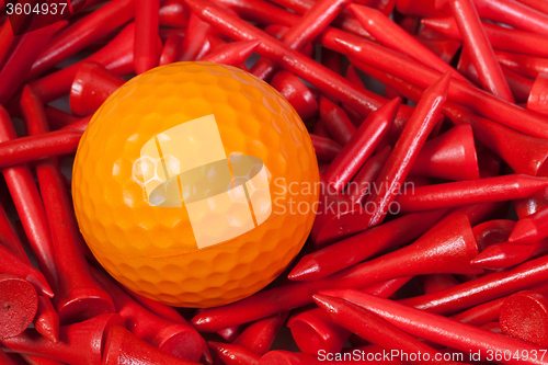 Image of Orange golf ball lying between wooden tees