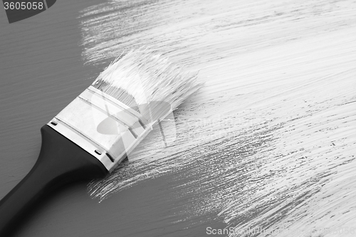 Image of Dirty paintbrush with white paint on half-painted board