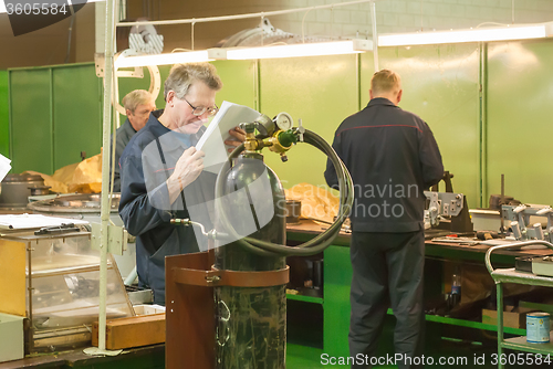 Image of Elderly mechanic reads drawing in shop