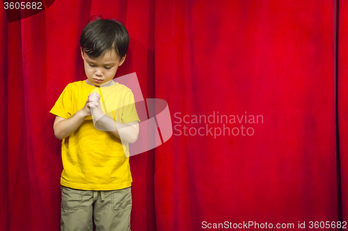 Image of Mixed Race Boy Praying in Front of Red Curtain