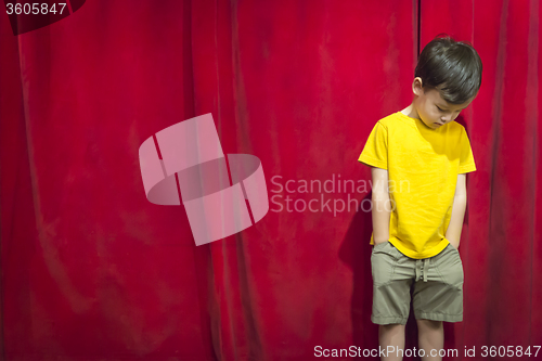 Image of Pouting Mixed Race Boy Standing In Front of Red Curtain