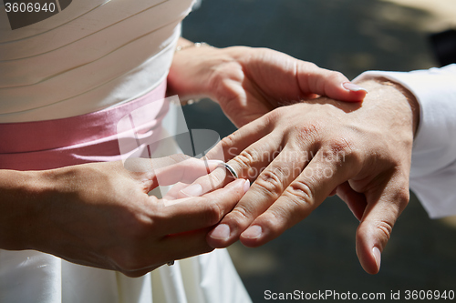 Image of bride puts ring on finger of groom