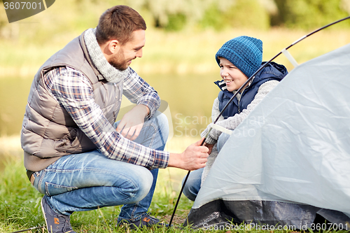 Image of happy father and son setting up tent outdoors