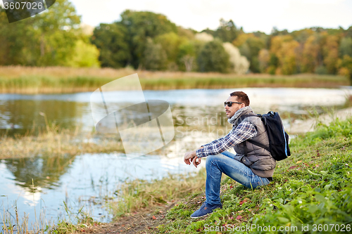 Image of man with backpack resting on river bank