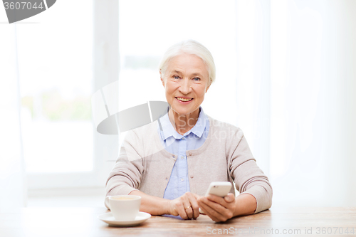 Image of senior woman with smartphone texting at home