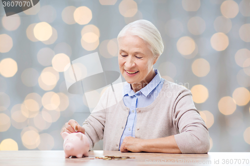 Image of senior woman putting money to piggy bank