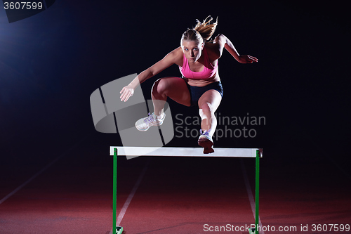 Image of woman athlete jumping over a hurdles