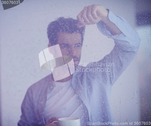 Image of relaxed young man drink first morning coffee withh rain drops on