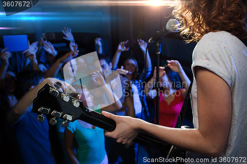 Image of female singer playing guitar over happy fans crowd