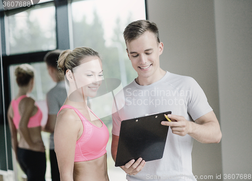 Image of smiling young woman with personal trainer in gym