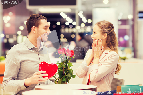 Image of happy couple with present and flowers in mall