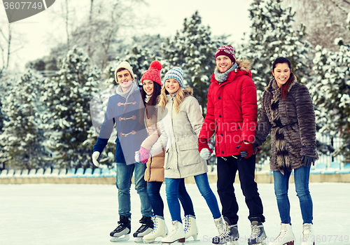 Image of happy friends ice skating on rink outdoors