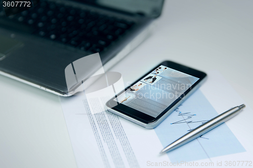 Image of close up of smartphone, laptop and pen on table