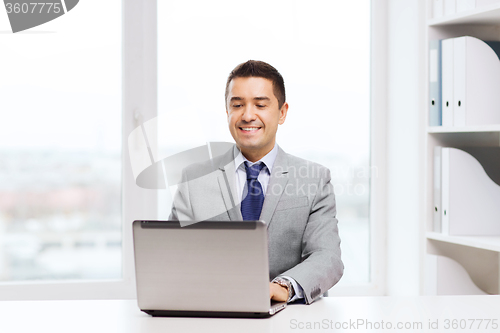 Image of happy businessman working with laptop in office