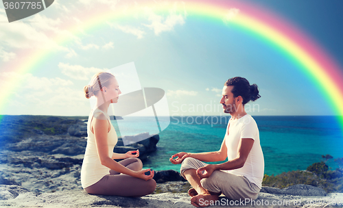Image of happy couple meditating in lotus pose on beach