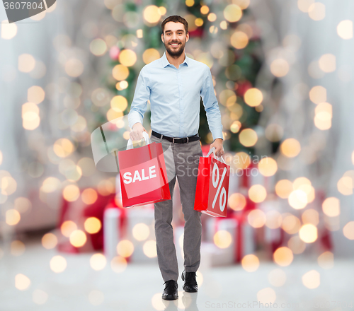 Image of happy man with shopping bags over christmas lights