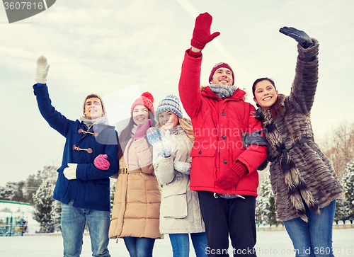 Image of happy friends waving hands on ice rink outdoors