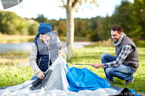 Image of happy father and son setting up tent outdoors