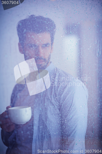 Image of relaxed young man drink first morning coffee withh rain drops on