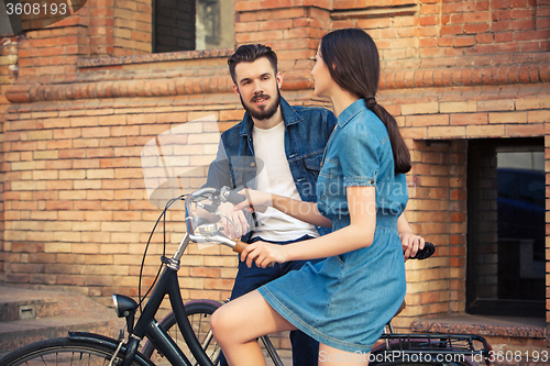 Image of Young couple sitting on a bicycle opposite city 