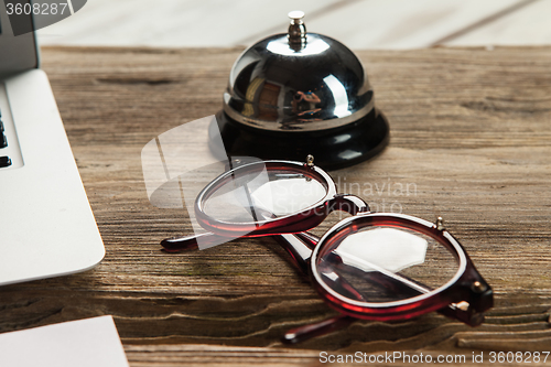 Image of The laptop, blank paper, glasses and small bell on the wooden table 