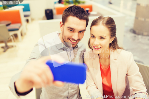 Image of happy couple taking selfie with smartphone in cafe