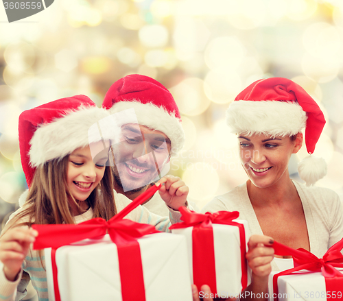 Image of happy family in santa hats sitting with gift boxes