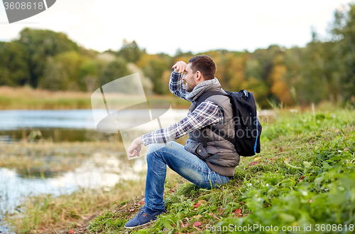 Image of smiling man with backpack resting on river bank