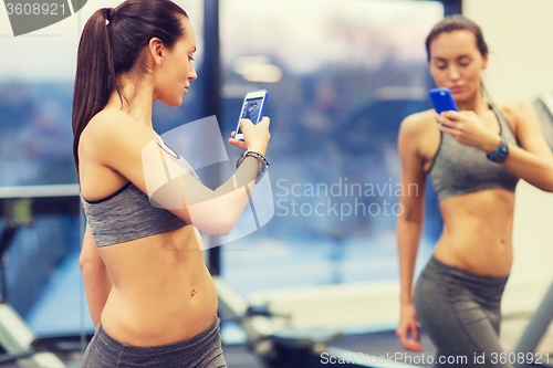 Image of woman with smartphone taking mirror selfie in gym