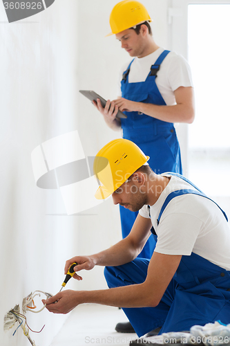 Image of builders with tablet pc and fixing wiring indoors