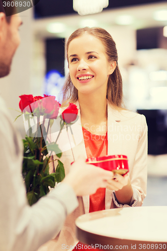 Image of happy couple with present and flowers in mall