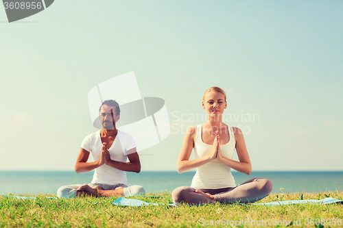 Image of smiling couple making yoga exercises outdoors