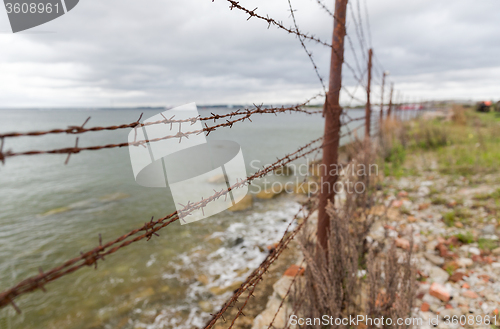 Image of barb wire fence over gray sky and sea