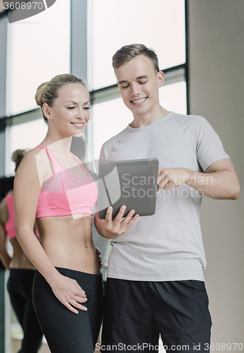 Image of smiling young woman with personal trainer in gym