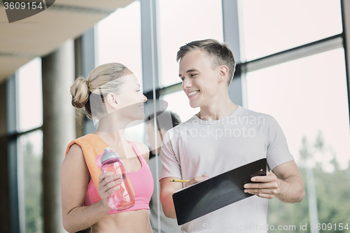 Image of smiling young woman with personal trainer in gym