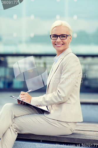 Image of young smiling businesswoman with notepad outdoors