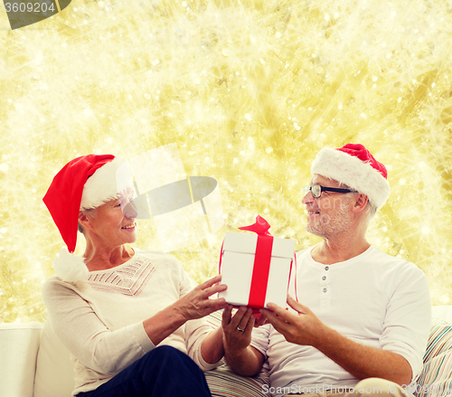 Image of happy senior couple in santa hats with gift box