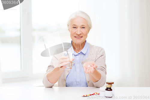 Image of happy senior woman with water and medicine at home