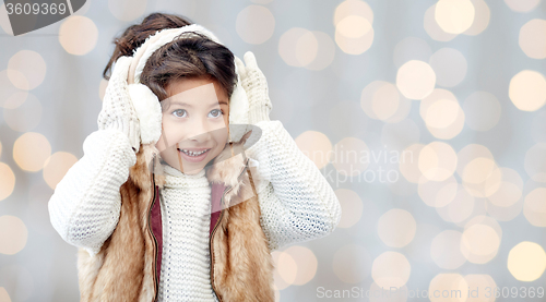 Image of happy little girl in earmuffs over holidays lights