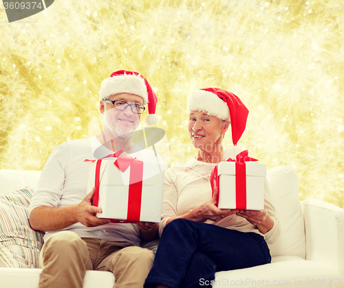 Image of happy senior couple in santa hats with gift boxes
