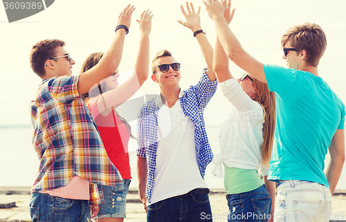 Image of group of smiling friends making high five outdoors