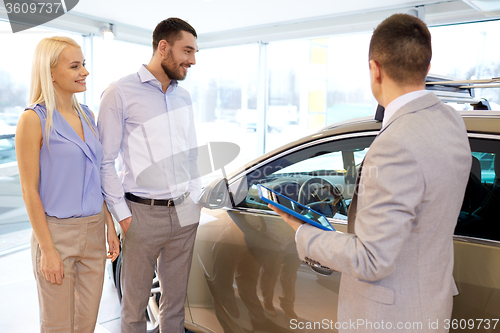 Image of happy couple with car dealer in auto show or salon