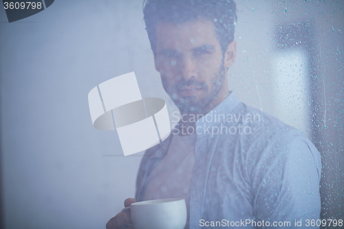 Image of relaxed young man drink first morning coffee withh rain drops on