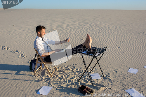 Image of Businessman using  laptop in a desert