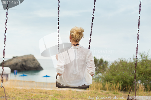 Image of Young blonde woman sitting on the swing