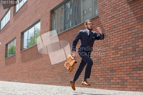 Image of young businessman running in a city street