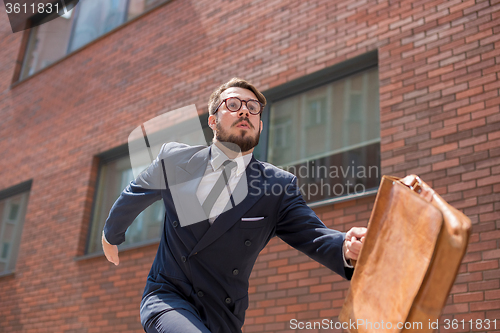 Image of young businessman running in a city street